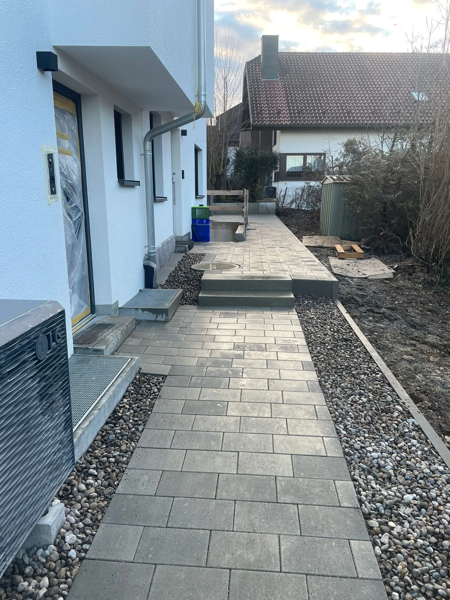 Plattenweg mit Kiesrändern entlang eines Wohnhauses